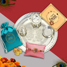 Raksha Bandhan gift with religiously themed Rakhi, silver thali, colored powders, and devotional message card.